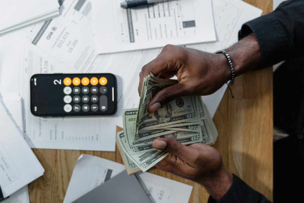 HR Services Person counting dollar bills over documents with a smartphone calculator on the desk.